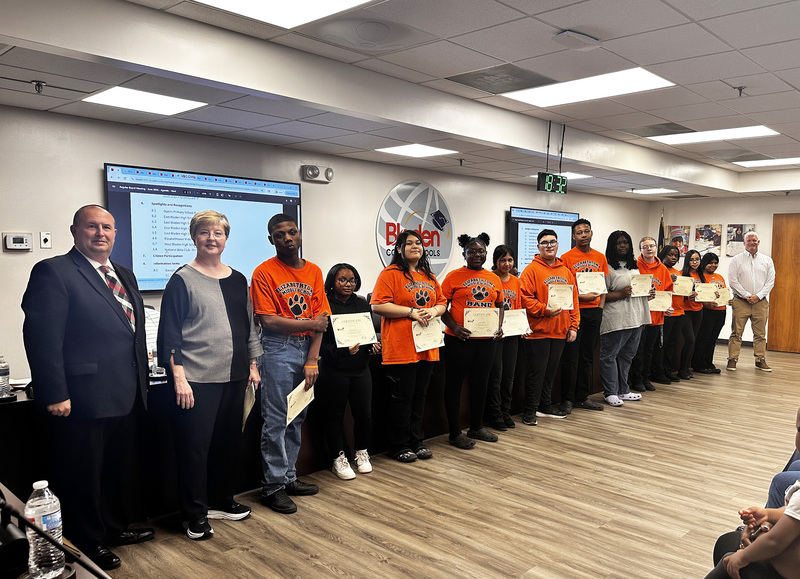 A group of Elizabethtown Middle School band students stand together in a board room with their band director, the superintendent and board chair.