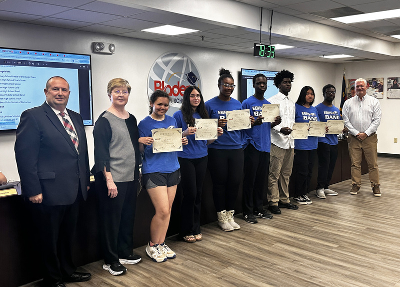 A group of band students from East Bladen High School stand together holding certificates, with their director, the superintendent and board chair.