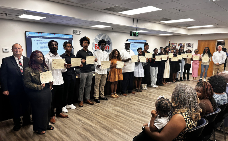 A group of high school track students stand with their coaches, the superintendent and board chair to be recognized for their success.