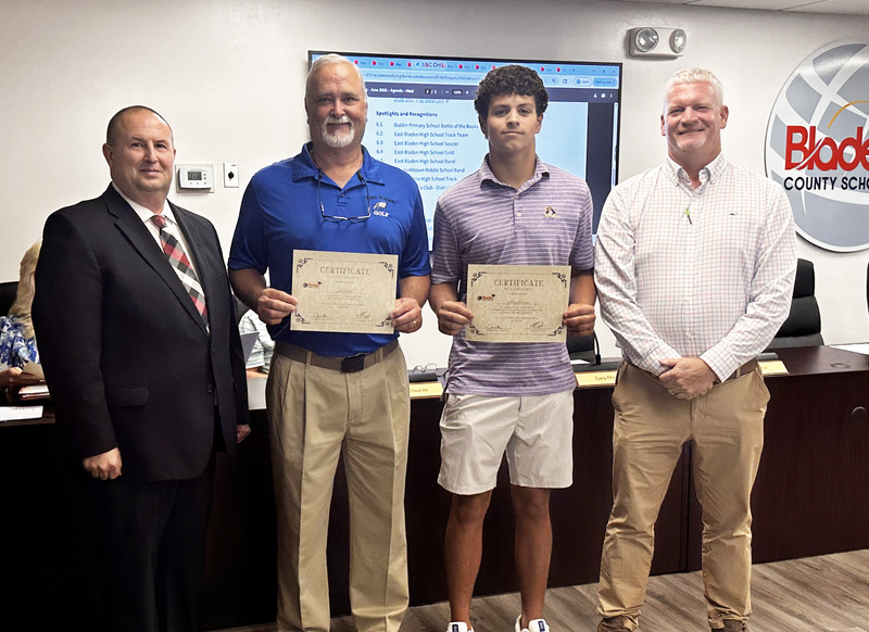 An East Bladen High School golf player stands with his coach, the superintendent, and board chair to be recognized for his success.