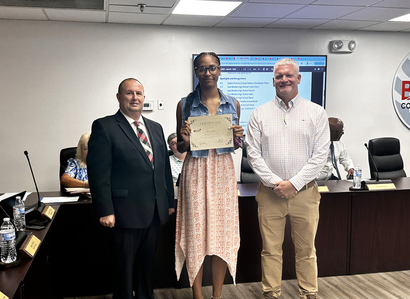 A West Bladen High School Track team member is standing with the superintendent and board chair to be recognized for their success with the team.