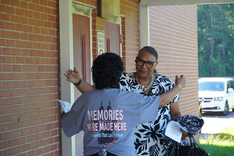 Two adults hug outside of a school building.