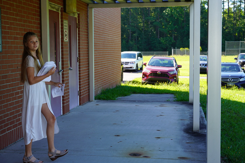 A student stands outside of a school building handing out event programs.