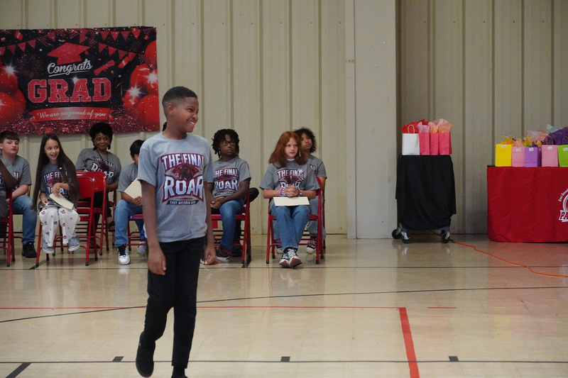 A student wearing an East Arcadia School shirt that says The Final Roar walks across a room smiling.