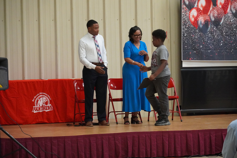 A student walks across the stage shaking hands with adults.