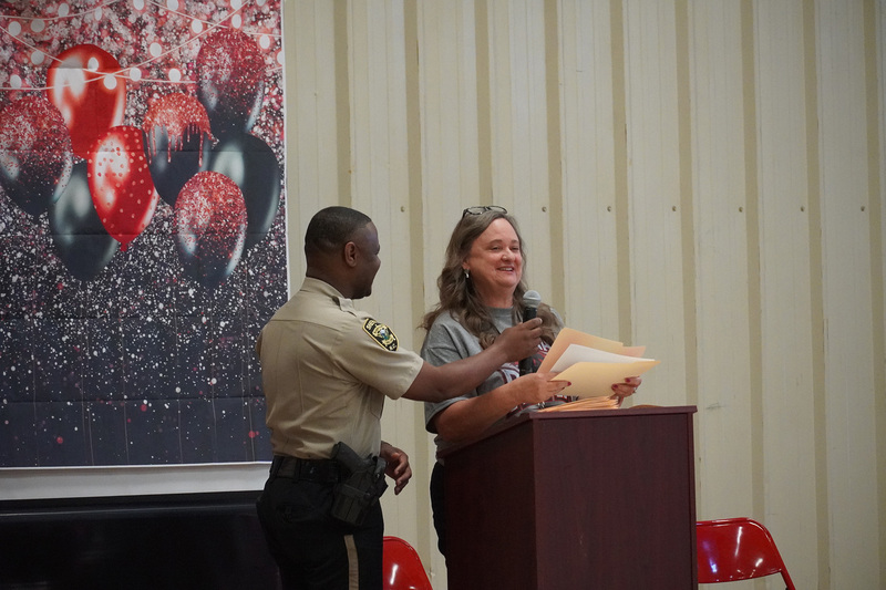A teacher stands at the podium while an SRO holds a microphone for her.