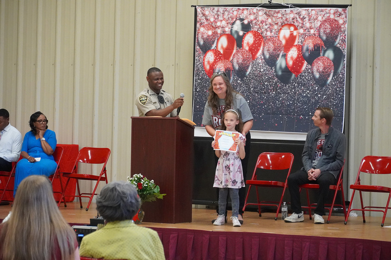 A teacher and a student who is holding a certificate, stand smiling on stage.