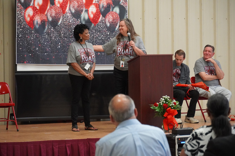 Two educators are on stage speaking at the podium.
