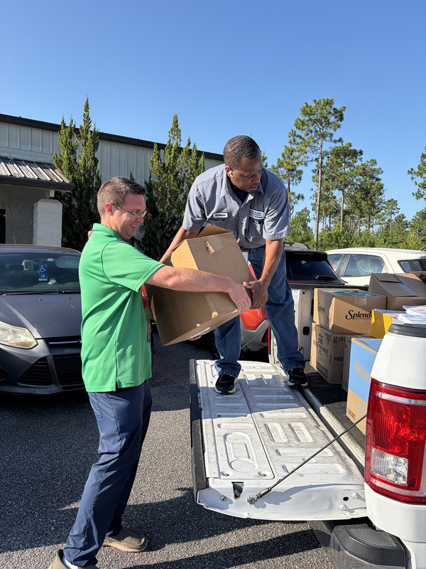 Two adults loading a box of supplies in the back of a pickup truck.