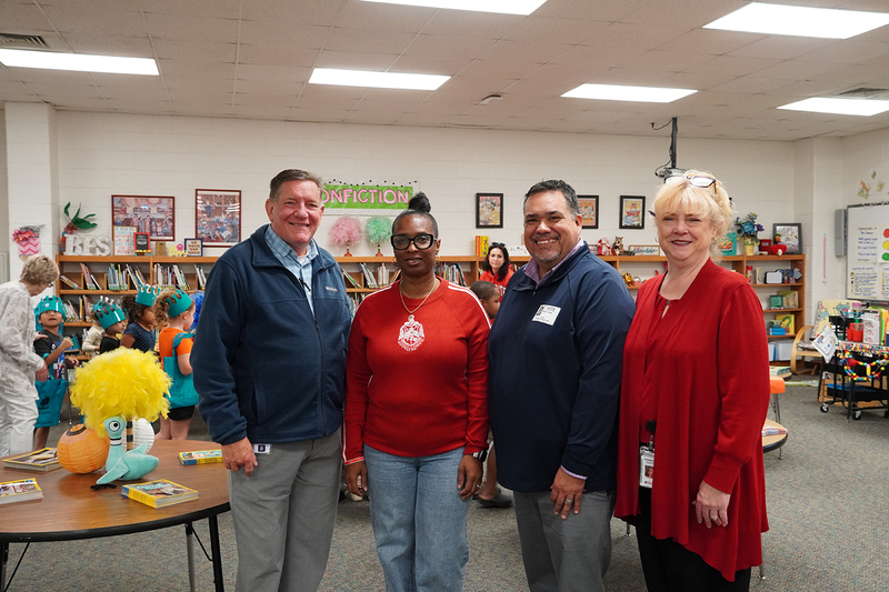 Four adults stand smiling in an elementary school library.