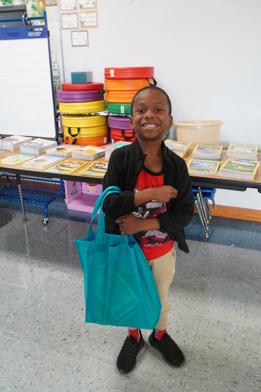An elementary aged student stands smiling in front of a table full of books.