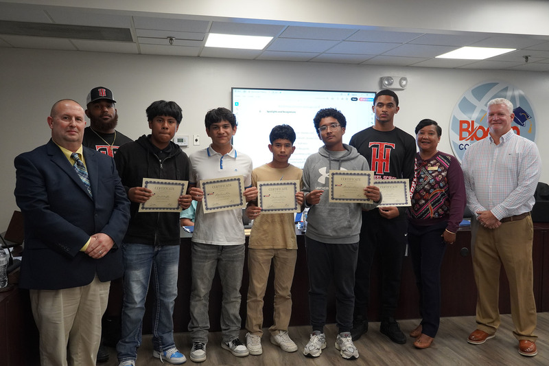 group of middle school boys stand together holding certificates with their coach, superintendent and board chair