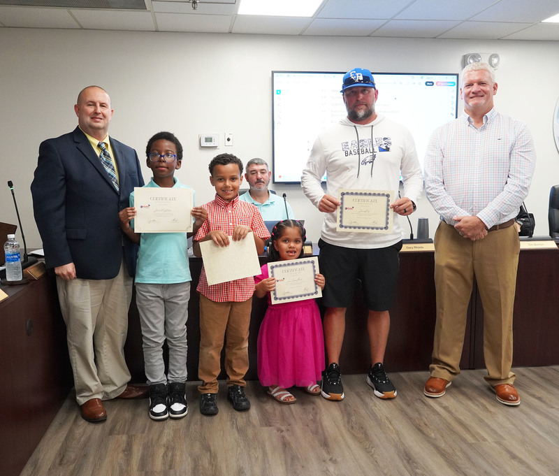 three students and one staff member stand holding certificates between the superintendnet and board chair