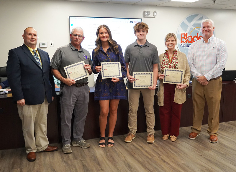 two employees and two staff members stand together holding certificates between the superintendent and board chair