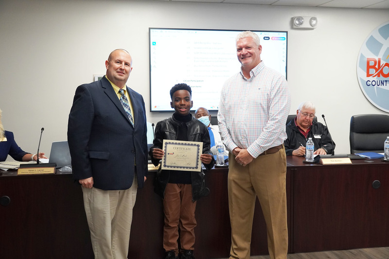 one student stand between the superintendent and board chair. the student is holding a certificate of recognition.