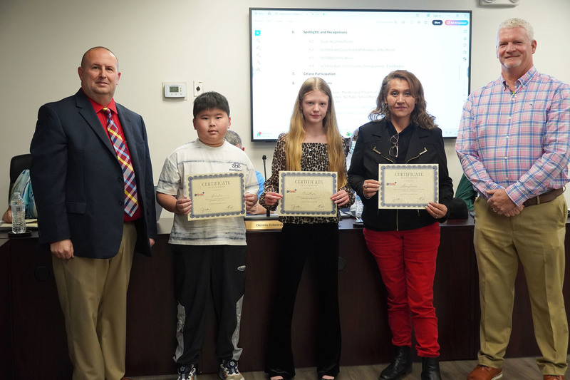 Two students and a staff member stand holding certificates with two administrators at a Bladen County Schools board meeting.