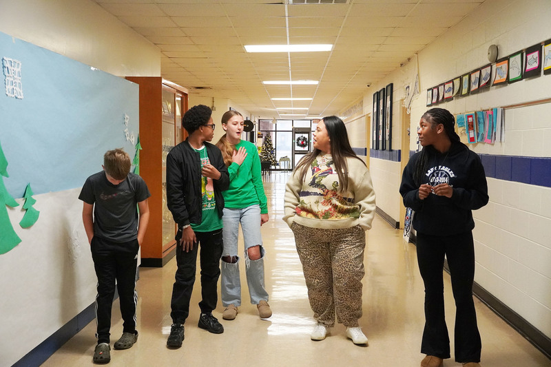 Teacher and students walk and talk together down a school hallway decorated with student artwork.