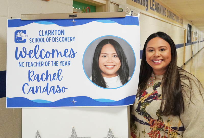 Teacher stands smiling beside a sign welcoming North Carolina Teacher of the Year Rachel Candaso at Clarkton School of Discovery.