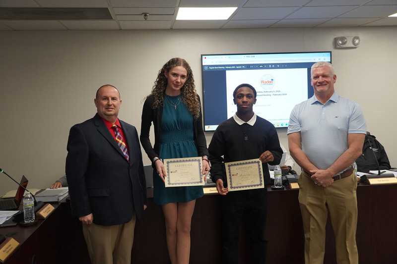 Two high school students stand with district leaders, each holding a certificate of recognition during a Bladen County Schools Board of Education meeting.