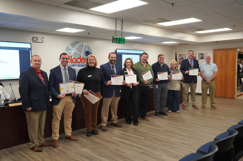 A group of educators stands with district leaders, each holding an Academic Growth Award certificate at a Bladen County Schools Board of Education meeting.