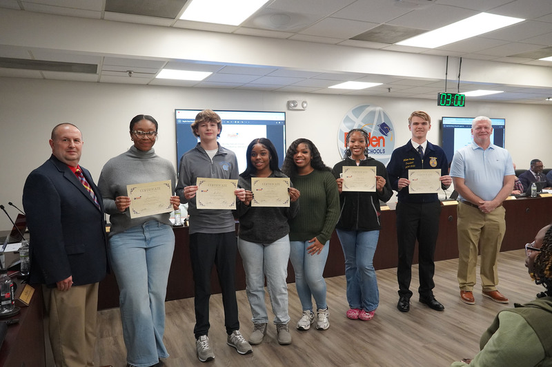A group of high school students stands with district leaders, each holding a certificate of recognition during a Bladen County Schools Board of Education meeting.