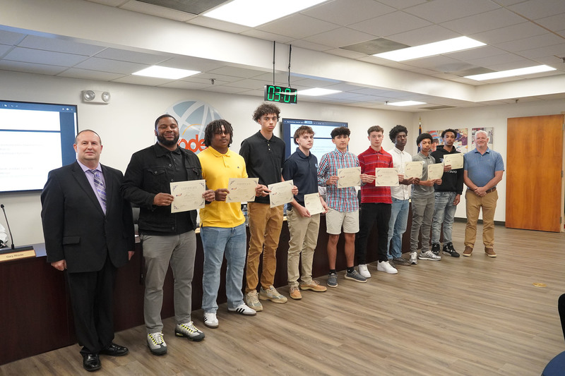 high school boys standing with three adults at board meeting holding certificates
