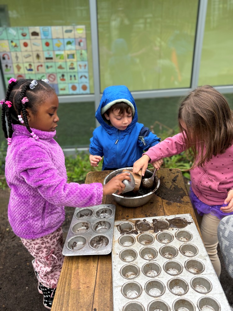 Three young children scooping dirt into muffin tins.