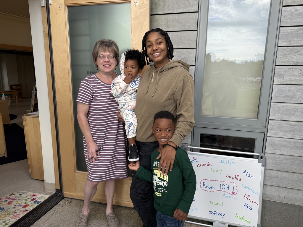Teacher taking a photo with child and his parent at classroom door.