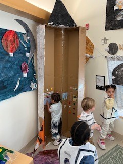 Young children playing with tall box desinged like a space ship.