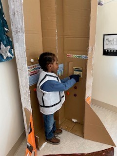 Young boy playing inside a make shift space ship pushing buttons on a calculator.