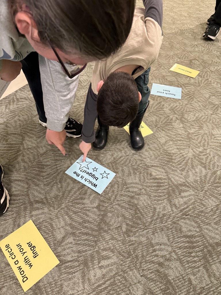 Child pointing to a card on the floor asking which one was the biggest.