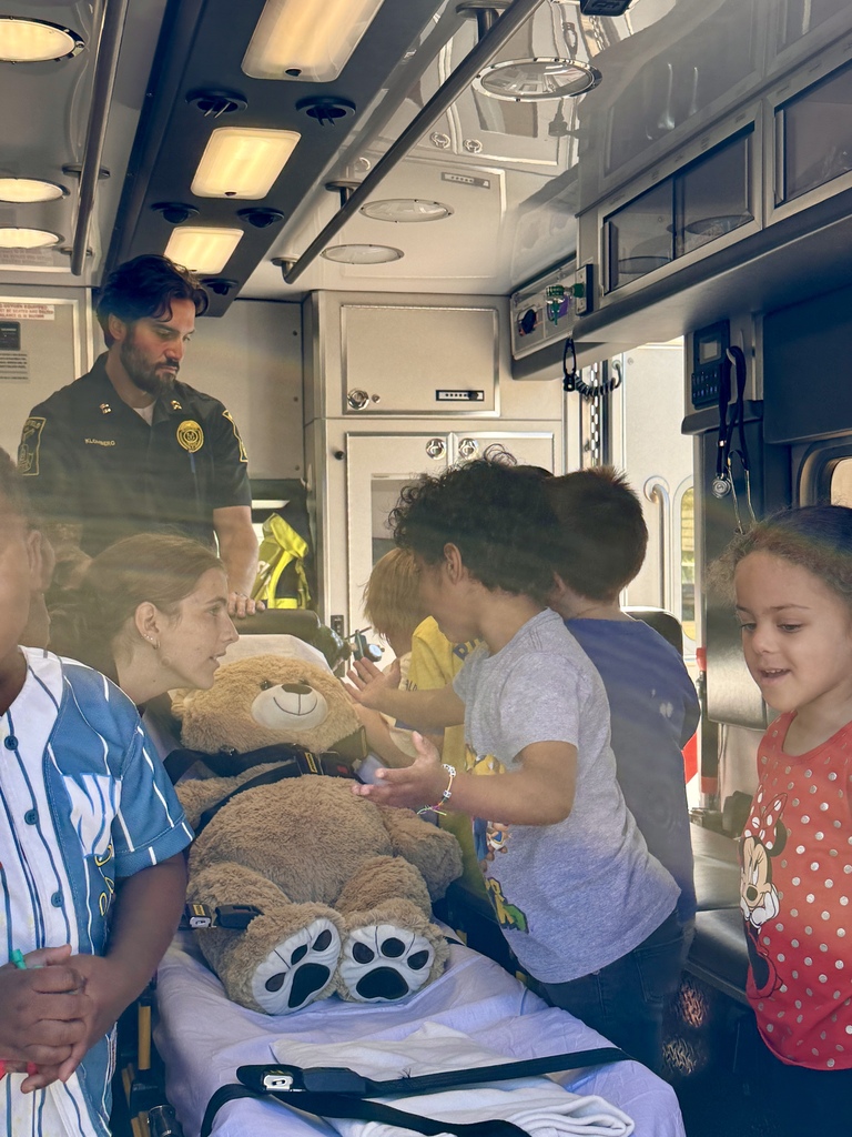Students inside an ambulance with a large teddy bear strapped on the bed.