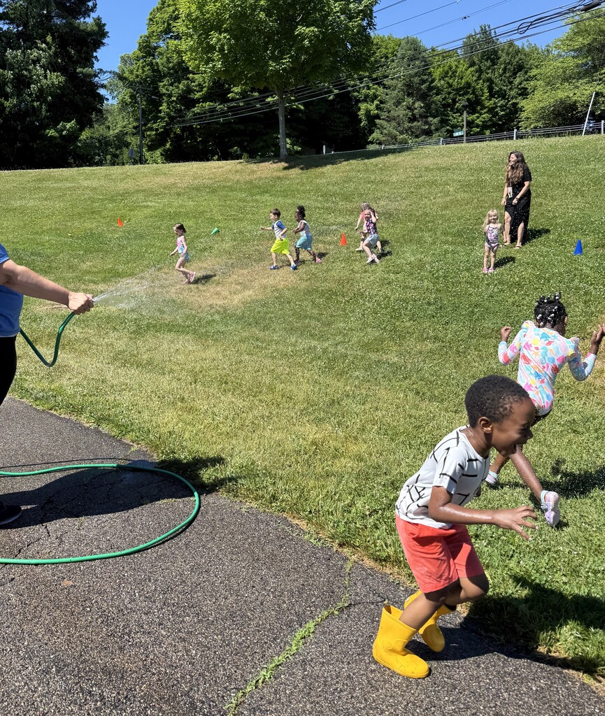 Young children running away from a sprinkler on  a hill.