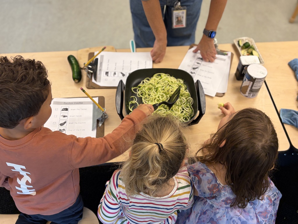 Three preschool children cooking zoodles in a pan.