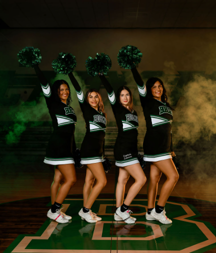 black and green background with green smoke, 4 cheerleaders pose with poms raised