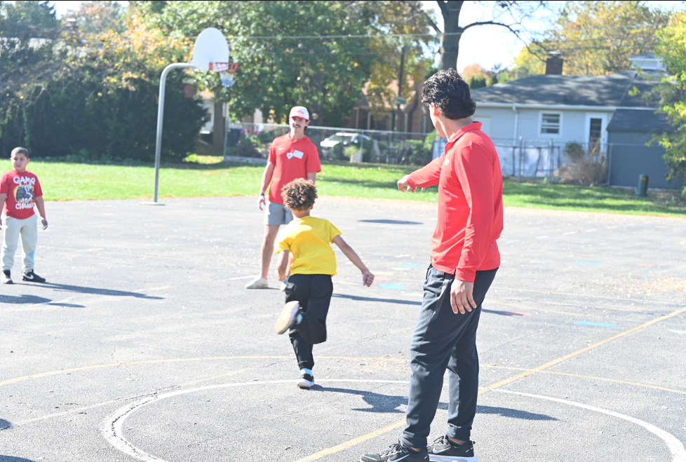 A man guides a child running in a circle on a basketball court with a hoop in the background.