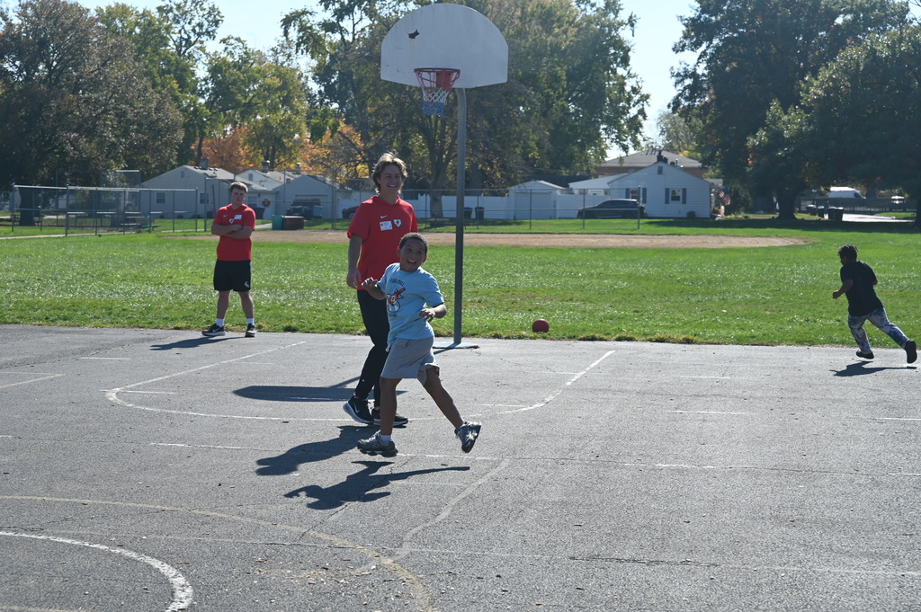 Four children play on a basketball court with one person in blue chasing another in red.