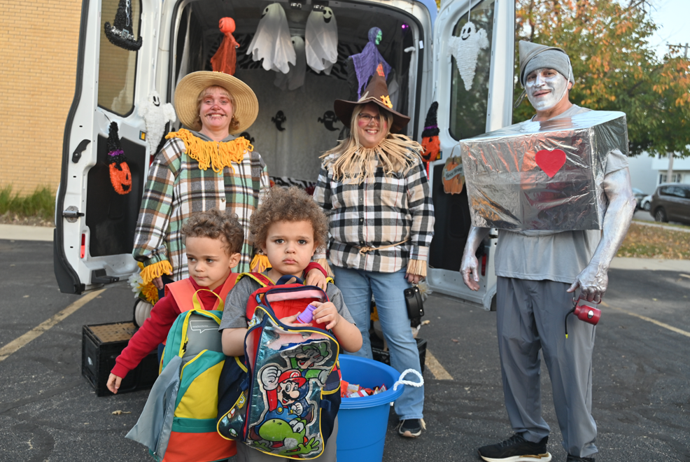 Five people in costumes stand in front of an open van; three hold buckets of candy.