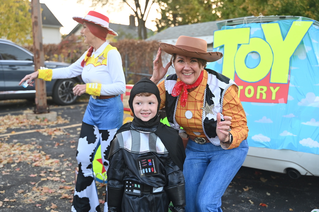 Three people in costumes standing near a Toy Story banner. One adult is crouching beside a child.
