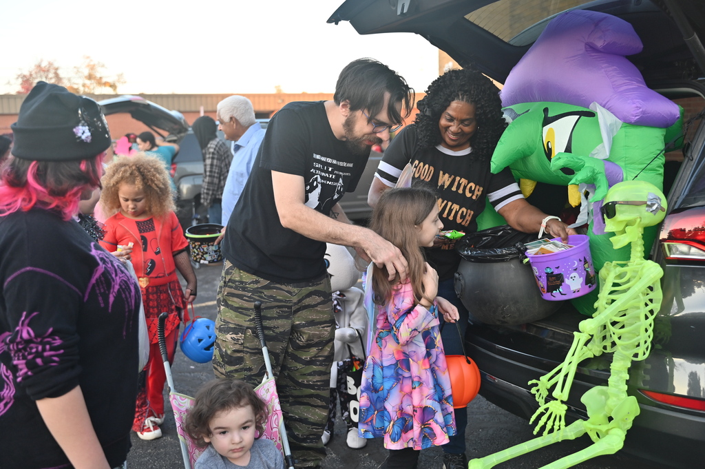 A group of people with children at an event. Adults help children take candy from a decorated vehicle.