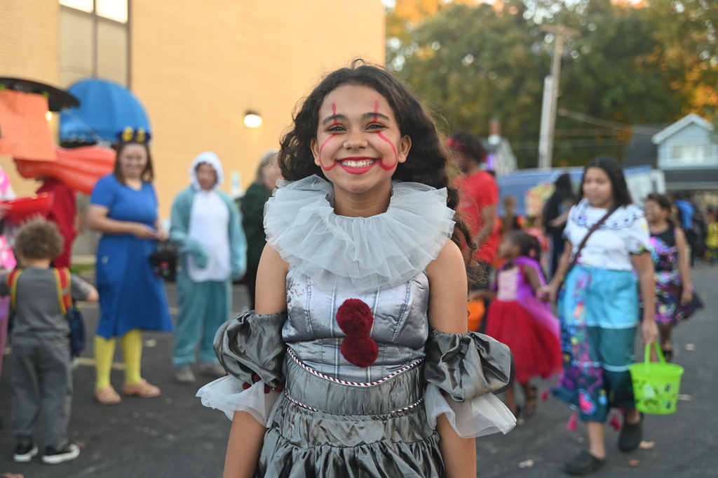 A young girl in a clown costume stands in the middle of a crowd of children.