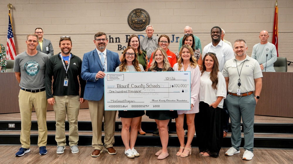 A group poses in the BCS boardroom holding an oversized $100,000 check from the Blount County Education Foundation to Blount County Schools for the Mini-Grant Program, dated October 1, 2026.
