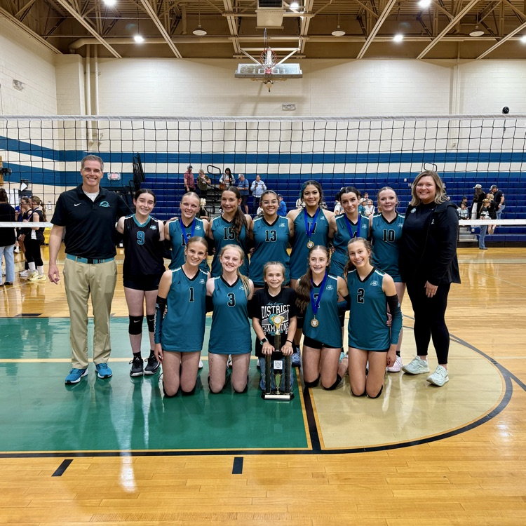 middle school volleyball team in front of net with trophy 