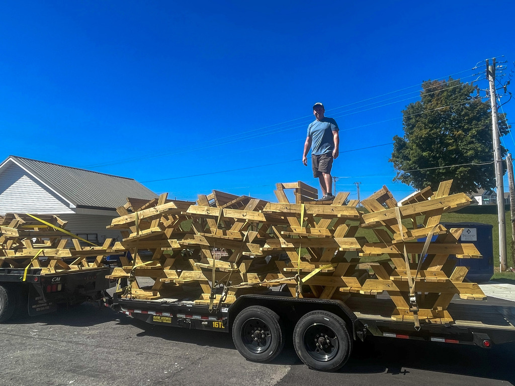A person stands beside stacked picnic tables secured on a trailer.