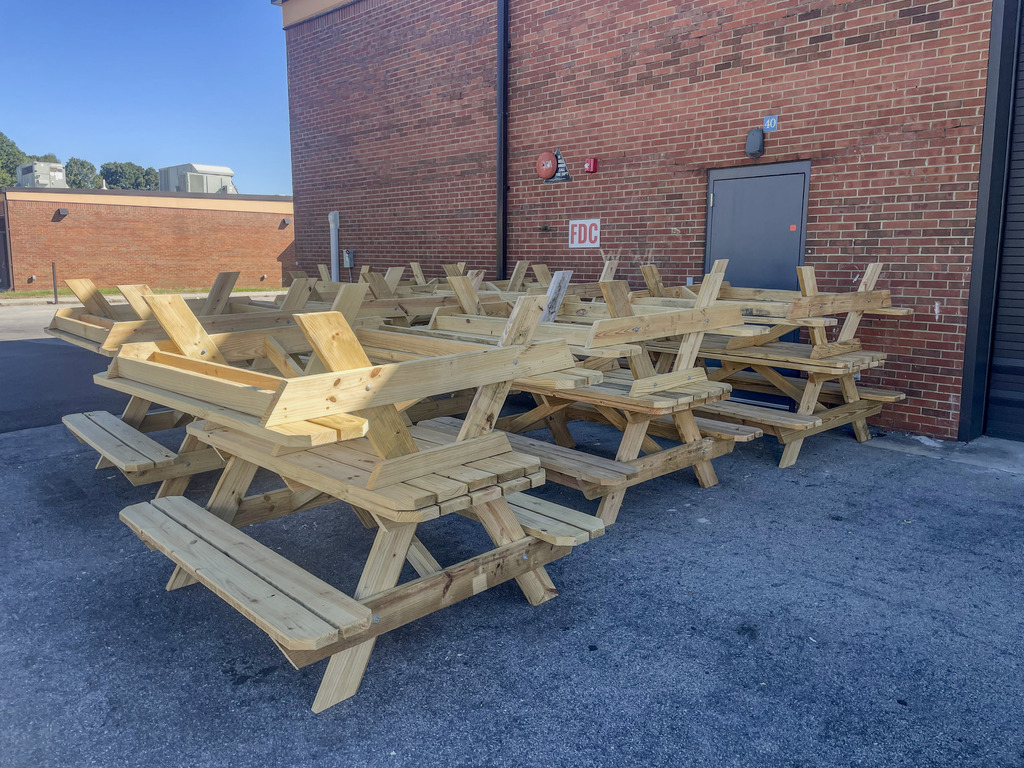 Newly built wooden picnic tables grouped outside a brick building.