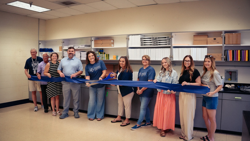 Blount County Schools staff and community partners stand together holding a blue ribbon during the grand opening ribbon-cutting ceremony for the BCS Teacher Depot.