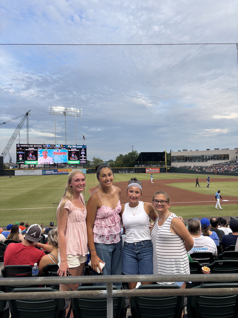 Four girls posed with a baseball field in the background