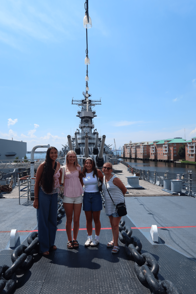 Four girls posed in front of a Navy ship