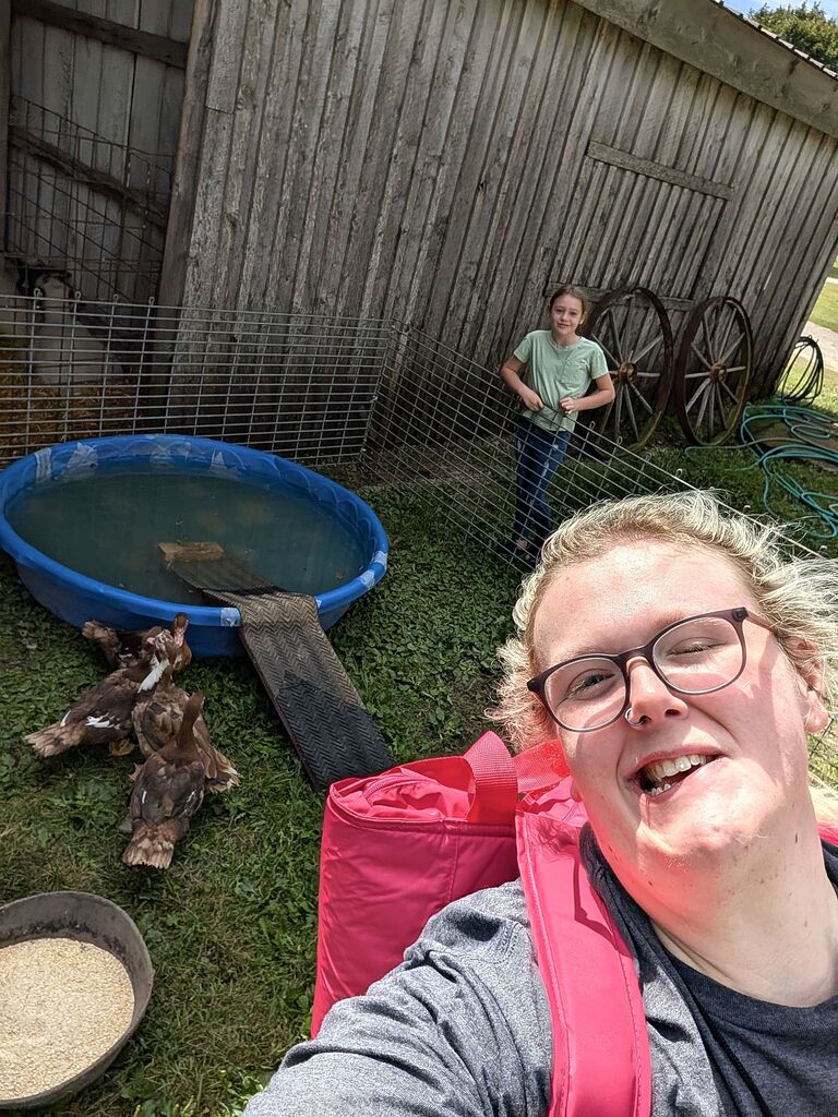 A teacher taking a selfie in front of the chickens with a student