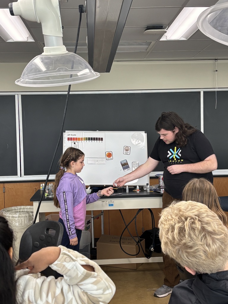 A student up in the front of a room getting something from the presenter.